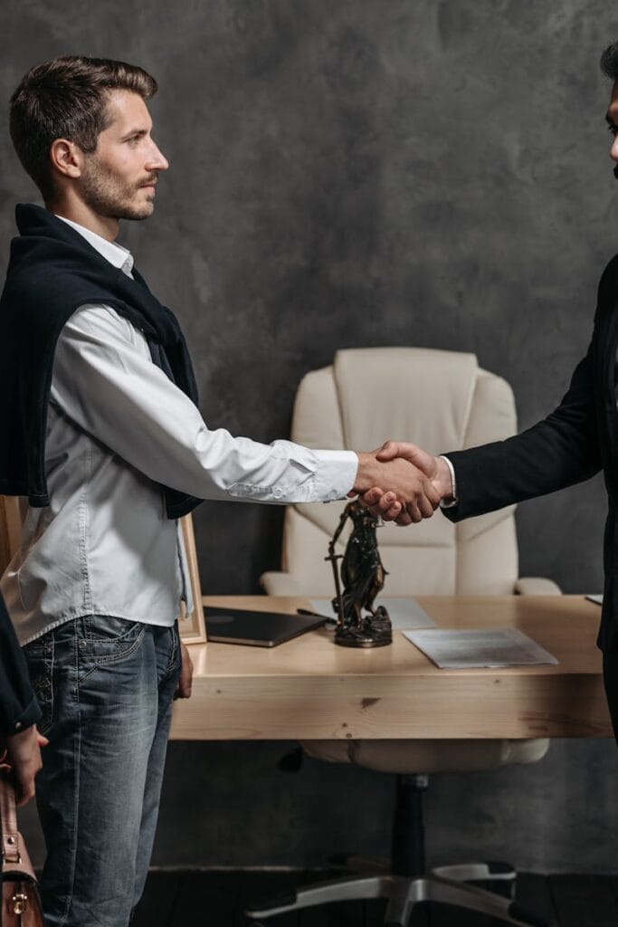 Three business professionals engage in a formal handshake in a modern office setting.